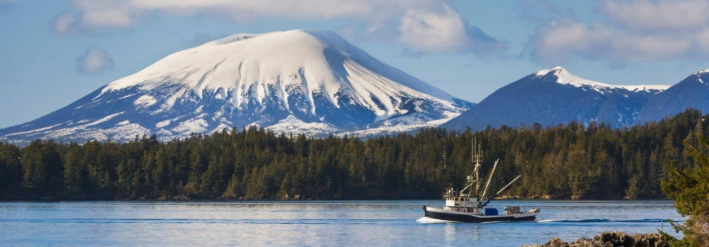A fishing boat trawling Sitka Sound in Alaskan waters with snow capped mountains in the background