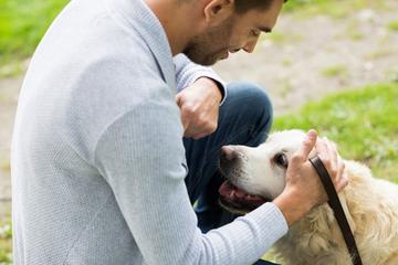 A man crouching down, looking into his dog's face while in a park