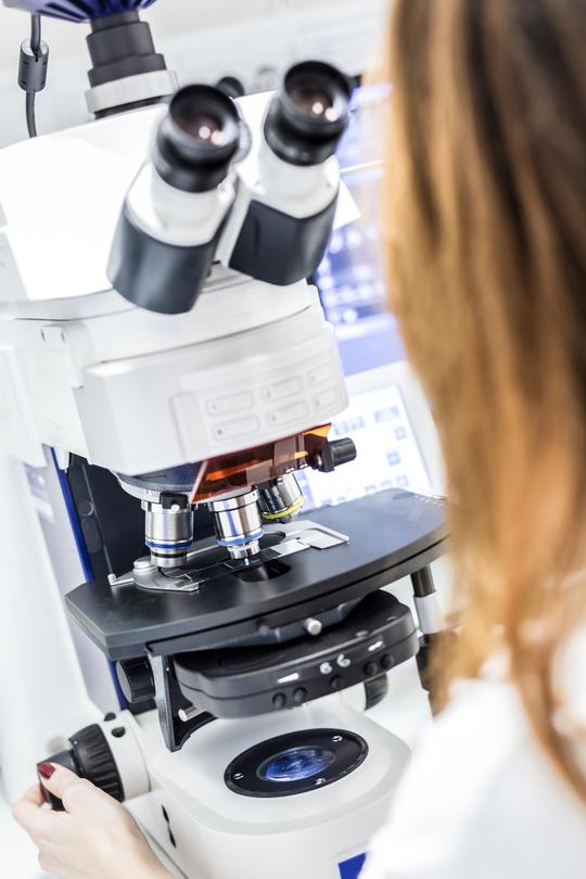 A view over the shoulder of a female scientist in front of a microscope